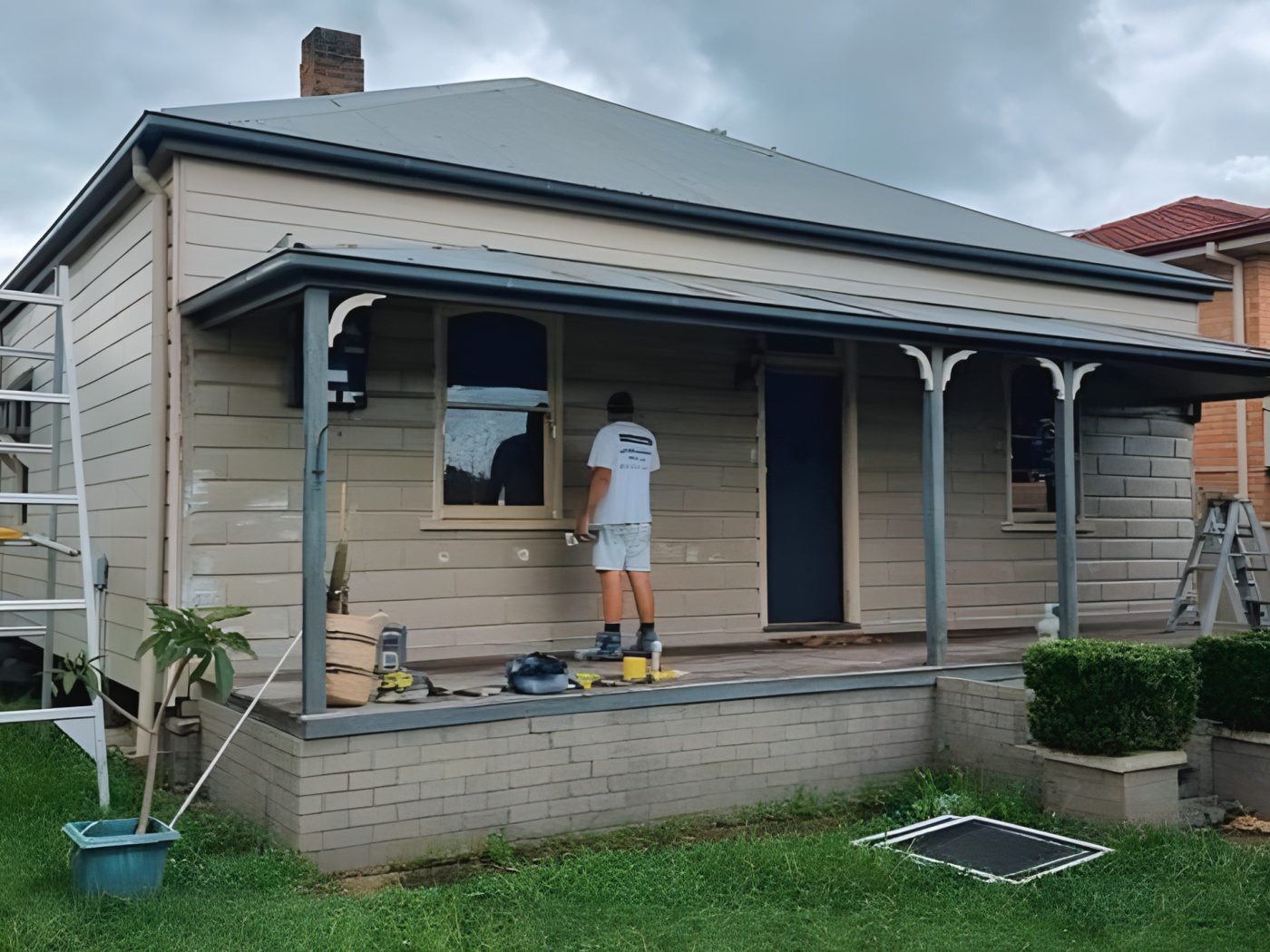Before: Weatherboard cottage before painting, with the old beige finish and repairs underway
