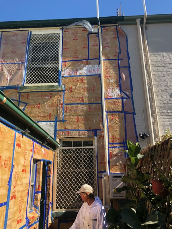 Specialist paint removal underway, with the wall wrapped and taped off for containment