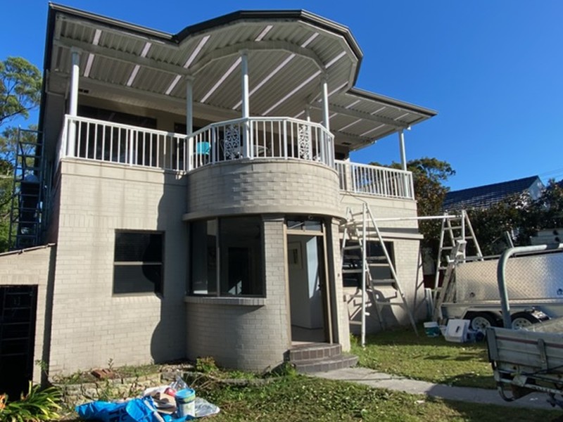Before: Two storey brick home before painting, in grey with ladders on site
