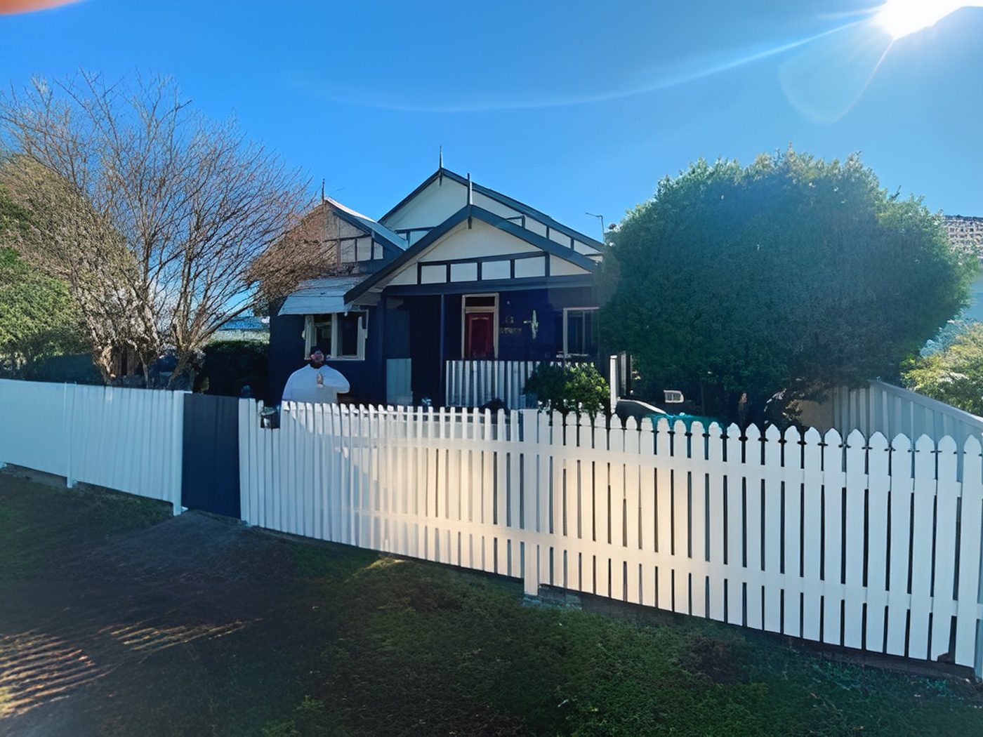 After: The same weatherboard home after restoration in deep blue with white trims and picket fence