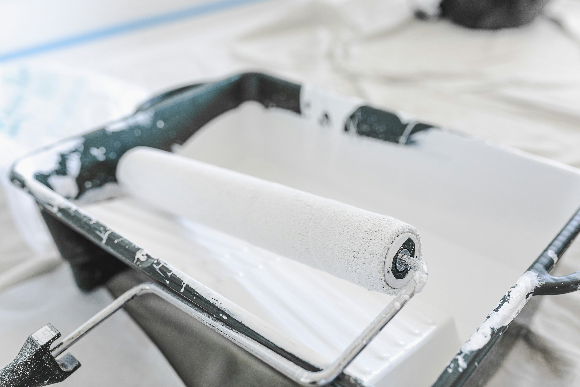 Paint roller loaded with white paint resting in a tray